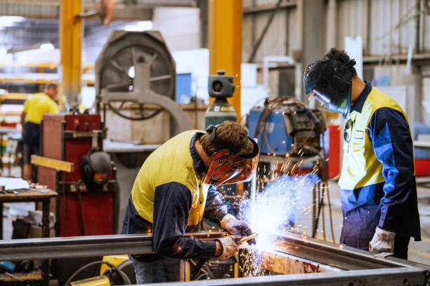 Large industrial warehouse with machinery and yellow support structures , with steel and metal processing equipment, welders welding steel bars